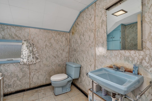 half bath with tile patterned flooring, vaulted ceiling, a sink, and toilet