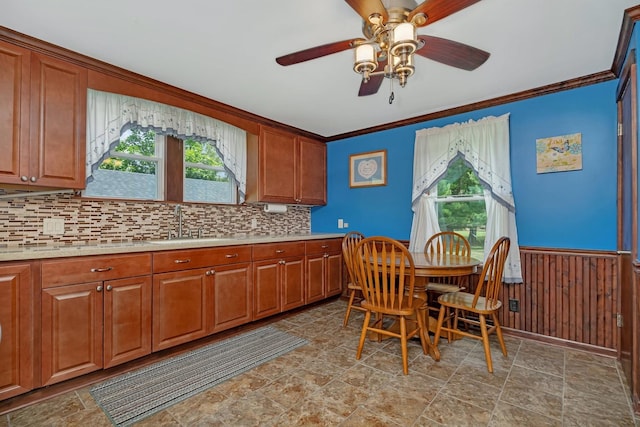 kitchen with brown cabinetry, wainscoting, ornamental molding, light countertops, and a sink