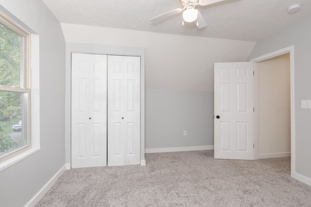 unfurnished bedroom featuring light carpet, a closet, lofted ceiling, and ceiling fan