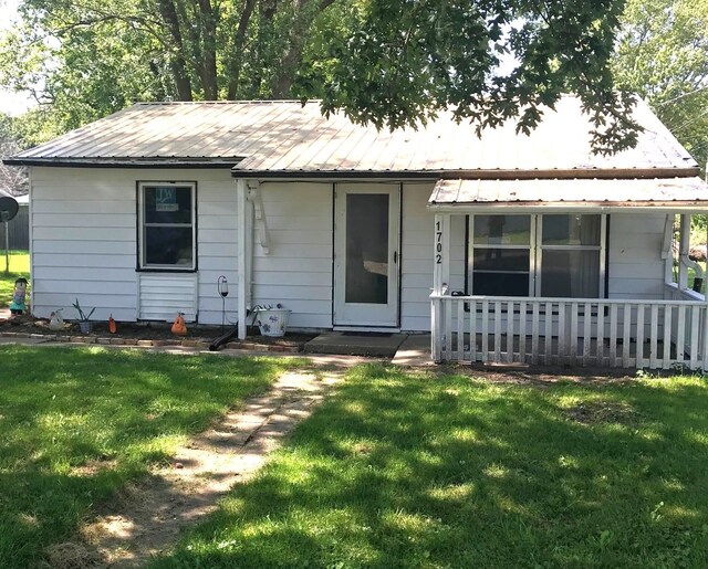 view of front of house with covered porch, metal roof, and a front lawn