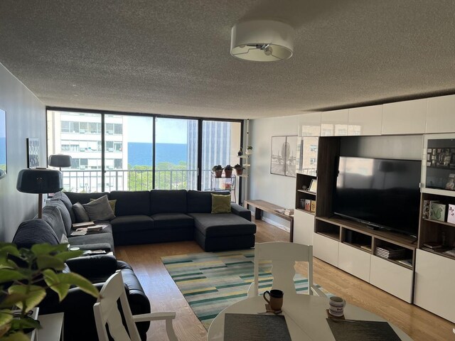 living room featuring light wood-type flooring, a textured ceiling, and a wall of windows