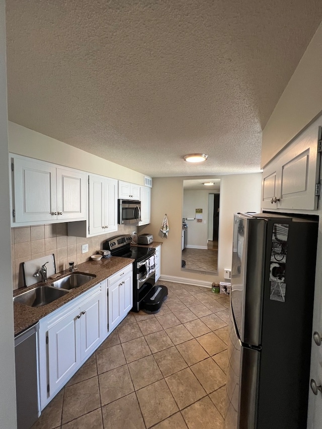 kitchen with a textured ceiling, light tile patterned floors, stainless steel appliances, sink, and white cabinets