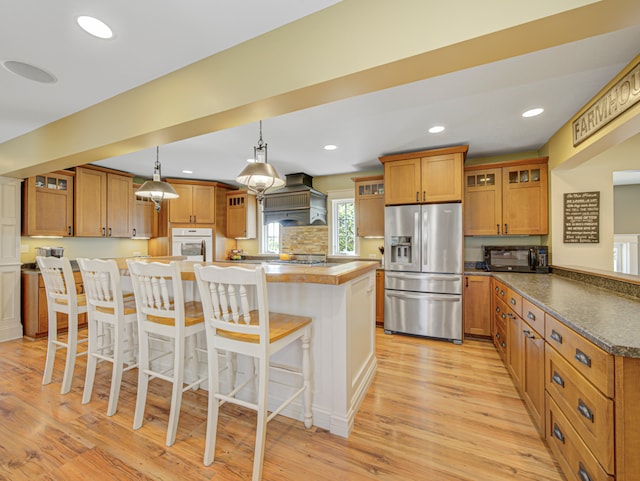 kitchen featuring a breakfast bar area, decorative light fixtures, appliances with stainless steel finishes, light hardwood / wood-style floors, and a center island