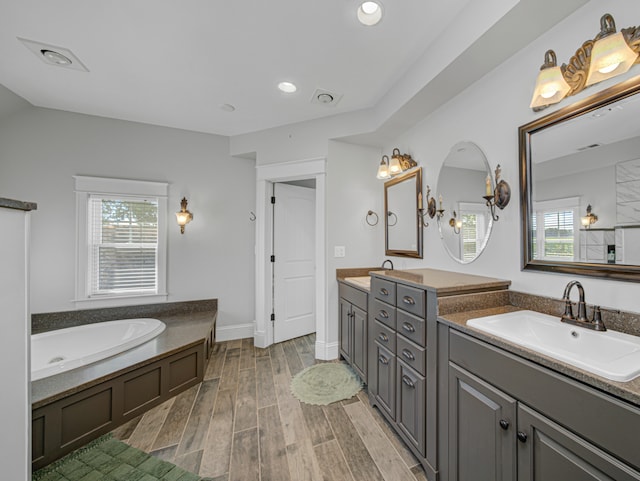 bathroom with hardwood / wood-style flooring, plenty of natural light, a washtub, and vanity