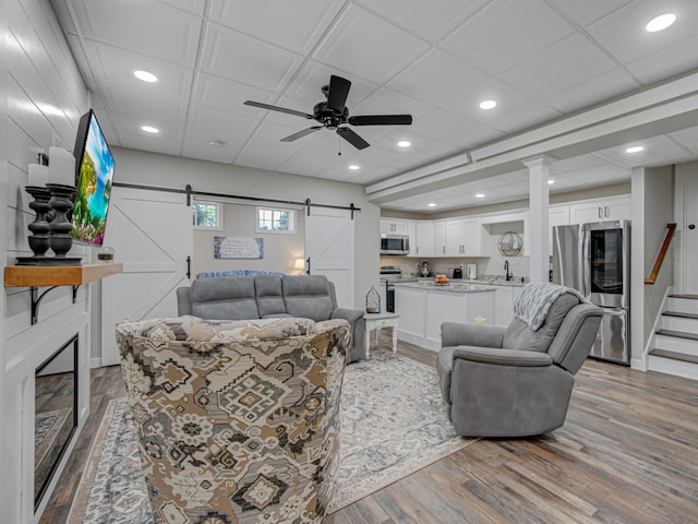 living room with a barn door, ceiling fan, sink, and light hardwood / wood-style flooring