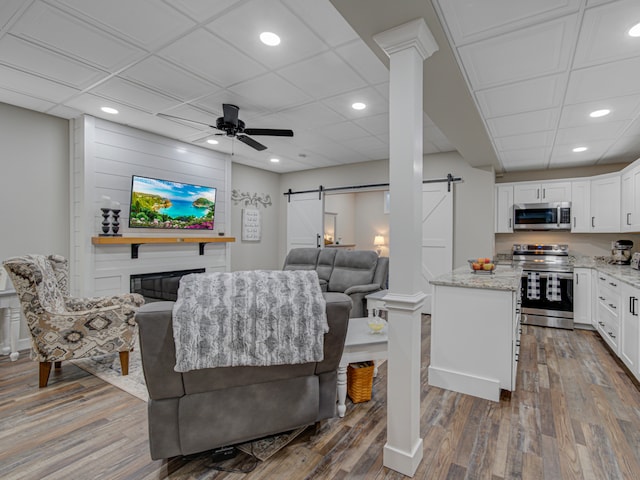 living room featuring a barn door, ceiling fan, a fireplace, and dark hardwood / wood-style floors