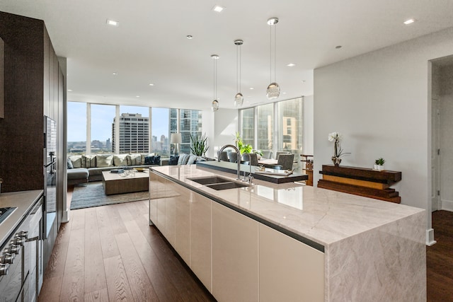 kitchen with a kitchen island with sink, pendant lighting, dark hardwood / wood-style flooring, sink, and white cabinets