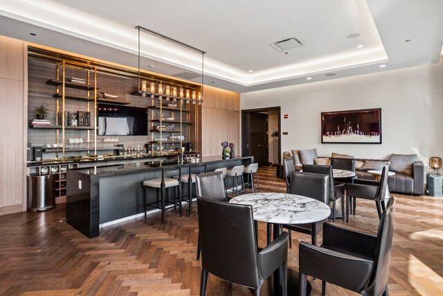 dining room with bar area, dark parquet flooring, and a raised ceiling