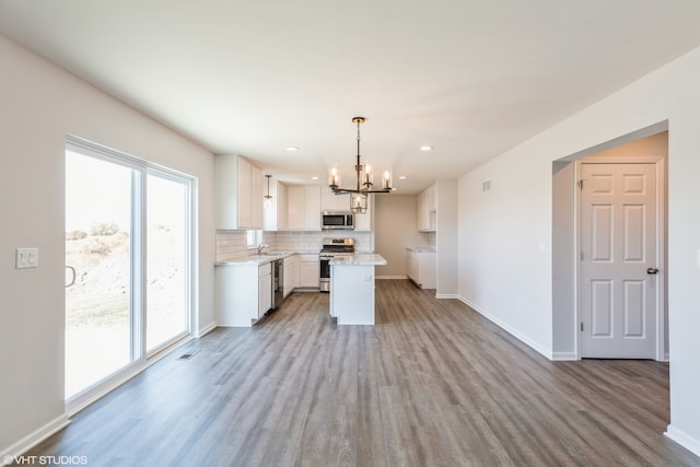 kitchen with a kitchen island, appliances with stainless steel finishes, white cabinetry, light hardwood / wood-style floors, and decorative light fixtures