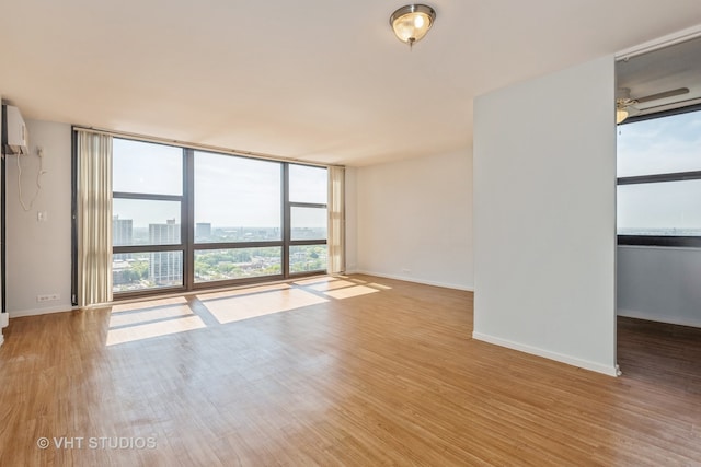 unfurnished room with light wood-type flooring, floor to ceiling windows, and a wall unit AC