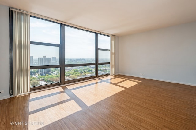 unfurnished room with a wall of windows and hardwood / wood-style floors