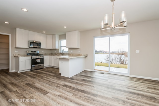 kitchen with appliances with stainless steel finishes, kitchen peninsula, hardwood / wood-style floors, pendant lighting, and white cabinets