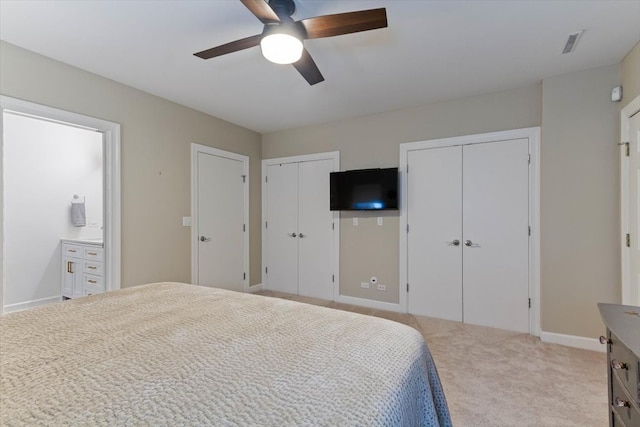 carpeted bedroom featuring ensuite bath, two closets, and ceiling fan