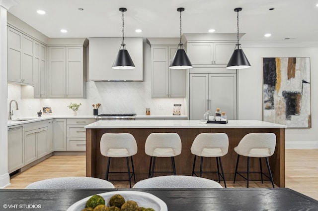 kitchen with light hardwood / wood-style floors, a kitchen island with sink, and hanging light fixtures