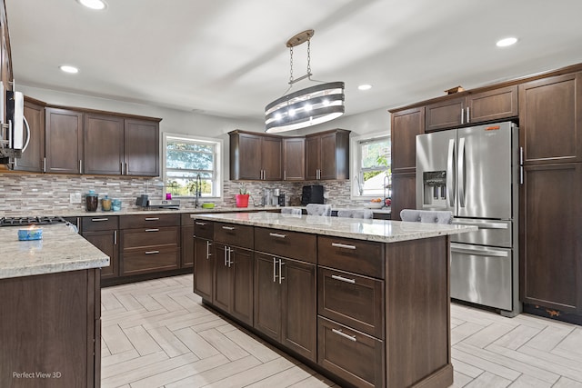 kitchen featuring dark brown cabinetry, a center island with sink, stainless steel appliances, and a kitchen bar