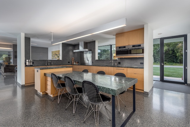 kitchen with decorative backsplash, wall chimney exhaust hood, a kitchen island, and stainless steel oven