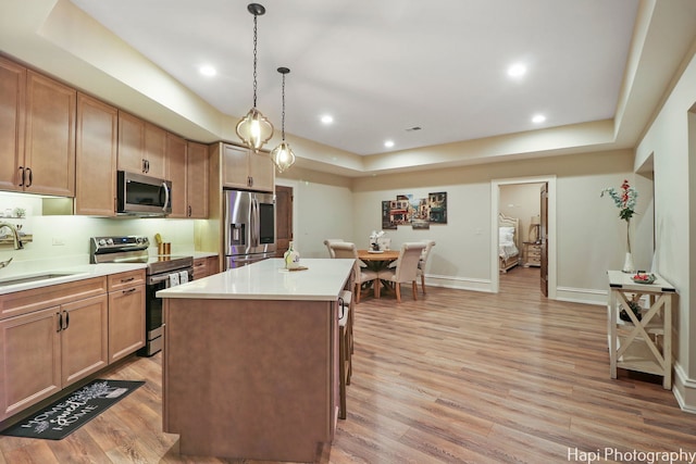 kitchen with a raised ceiling, light wood-type flooring, sink, and appliances with stainless steel finishes