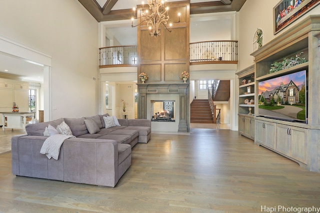 living room featuring a multi sided fireplace, an inviting chandelier, a high ceiling, and light hardwood / wood-style floors