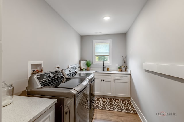 washroom featuring cabinets, sink, washer and dryer, and light hardwood / wood-style floors