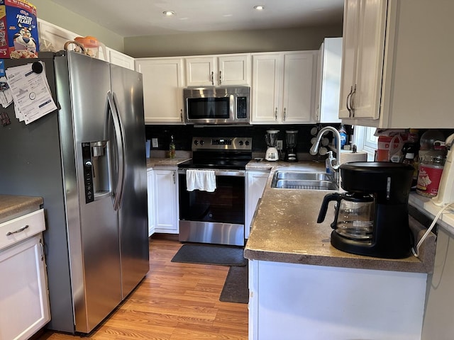 kitchen with appliances with stainless steel finishes, a sink, light wood-style flooring, and white cabinetry