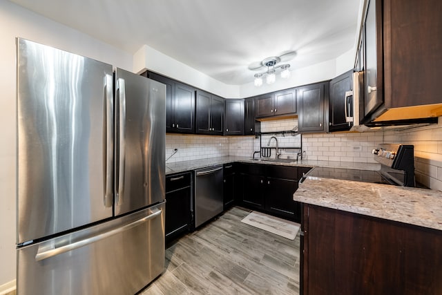 kitchen featuring light wood-type flooring, tasteful backsplash, light stone counters, sink, and appliances with stainless steel finishes