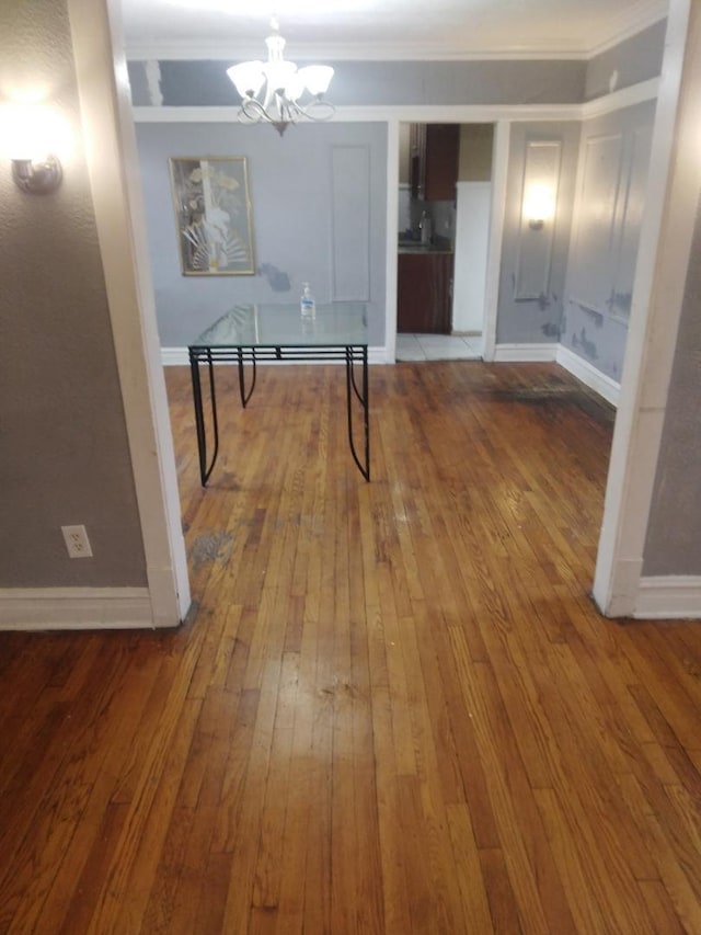unfurnished dining area featuring hardwood / wood-style floors, baseboards, an inviting chandelier, and crown molding