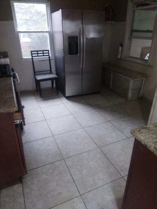 kitchen with light tile patterned floors, light stone counters, and stainless steel fridge with ice dispenser