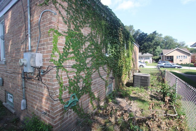 view of side of property featuring central AC unit, fence, and brick siding