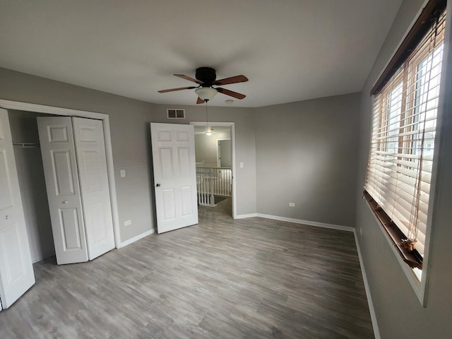 unfurnished bedroom with a closet, visible vents, ceiling fan, wood finished floors, and baseboards