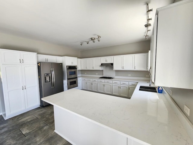 kitchen with white cabinets, light stone counters, a peninsula, stainless steel appliances, and a sink