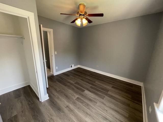 unfurnished bedroom featuring a ceiling fan, visible vents, baseboards, dark wood-type flooring, and a closet
