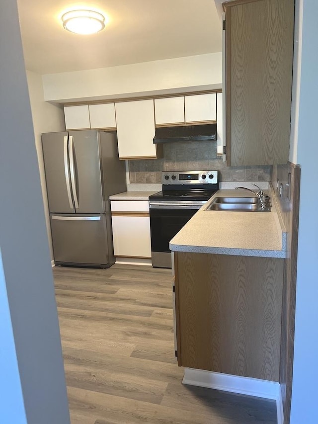 kitchen featuring white cabinets, appliances with stainless steel finishes, under cabinet range hood, a sink, and light wood-type flooring