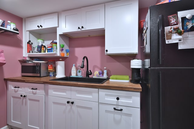 kitchen with white cabinets, black refrigerator, sink, and wood counters