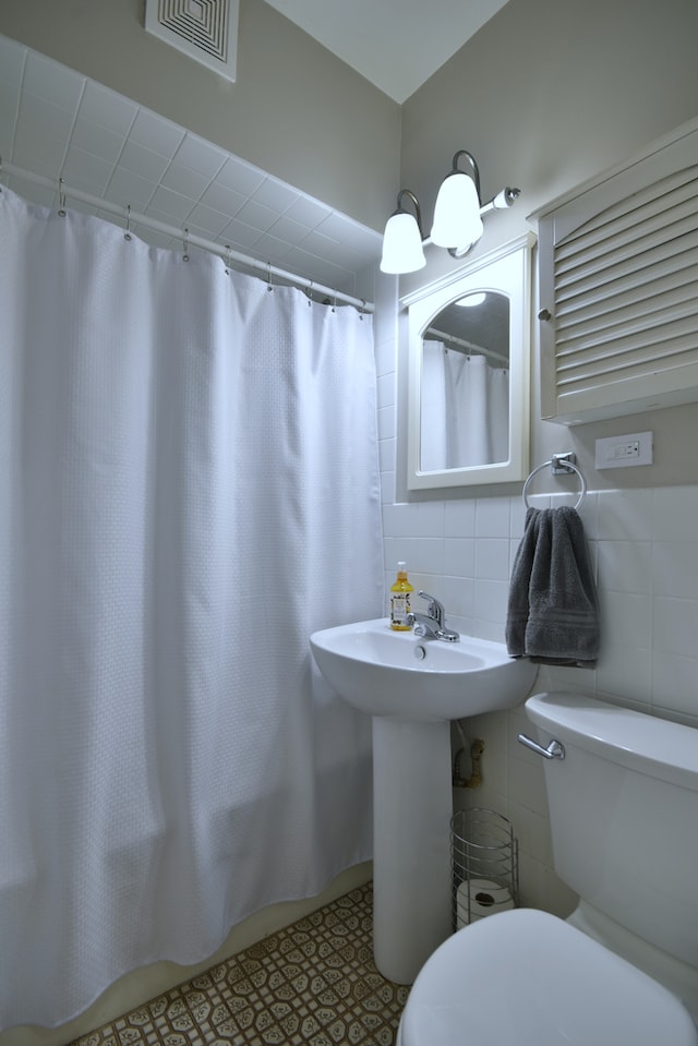 bathroom featuring tile walls, toilet, and walk in shower