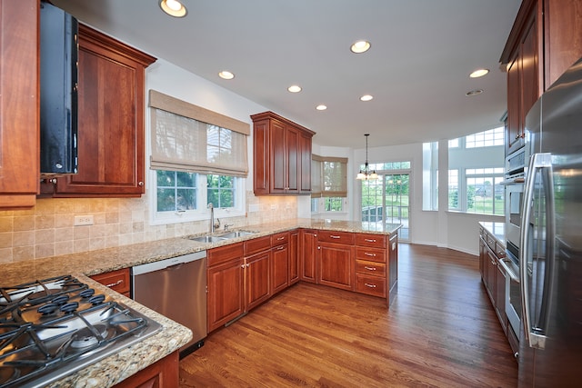 kitchen with hardwood / wood-style floors, backsplash, appliances with stainless steel finishes, kitchen peninsula, and sink