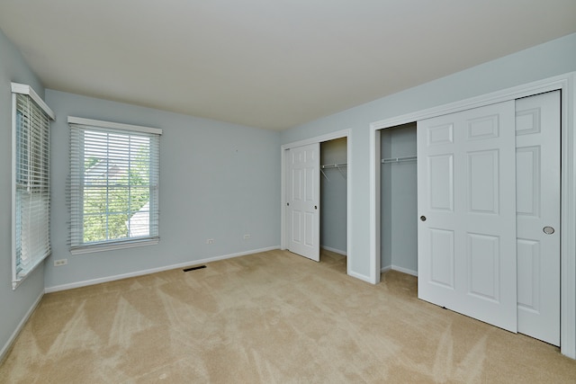 unfurnished bedroom featuring light carpet and multiple closets