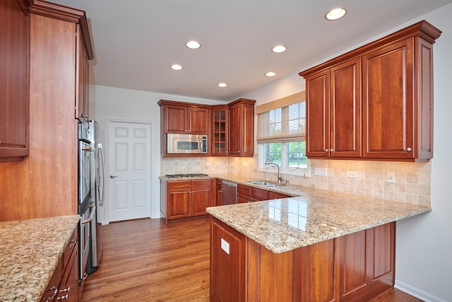 kitchen with light stone countertops, light hardwood / wood-style flooring, appliances with stainless steel finishes, kitchen peninsula, and sink