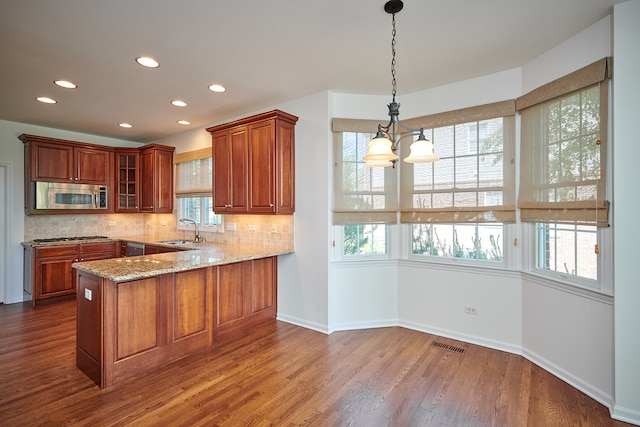 kitchen featuring hardwood / wood-style floors, appliances with stainless steel finishes, light stone countertops, a chandelier, and kitchen peninsula