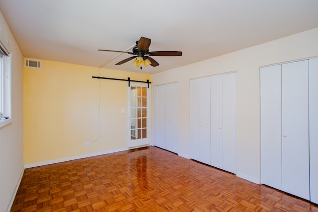 unfurnished bedroom with parquet floors, a barn door, and multiple closets