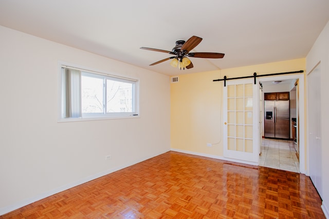 empty room with light parquet flooring, ceiling fan, and a barn door