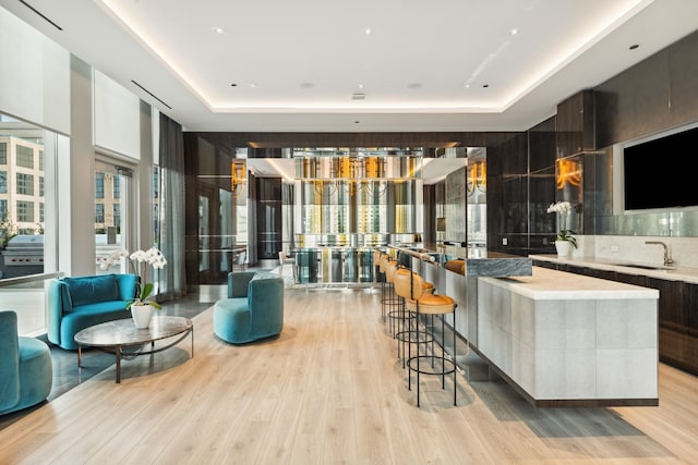 living room with light hardwood / wood-style flooring, a raised ceiling, and wet bar