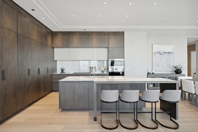 kitchen featuring a kitchen breakfast bar, light hardwood / wood-style flooring, decorative backsplash, light stone counters, and a large island