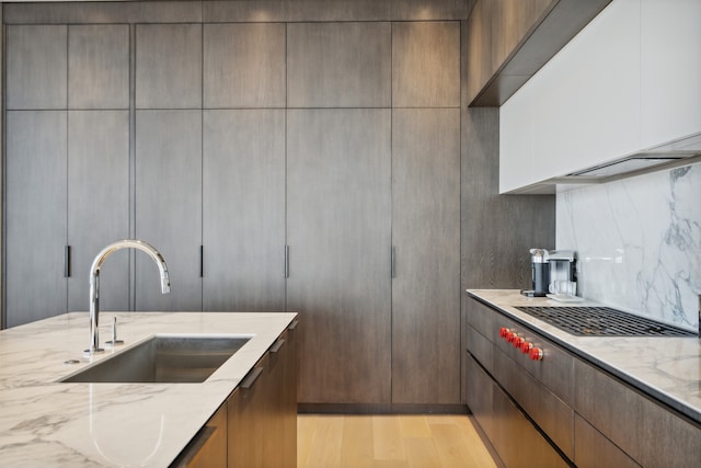 kitchen with stainless steel gas cooktop, sink, decorative backsplash, light stone counters, and light wood-type flooring