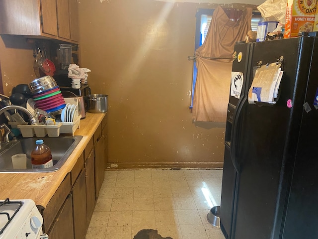 kitchen with black fridge, white range, light tile patterned floors, and sink