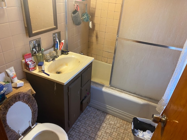 full bathroom with vanity, combined bath / shower with glass door, tile patterned flooring, tile walls, and toilet