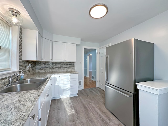 kitchen with white cabinets, light wood-type flooring, stainless steel refrigerator, sink, and tasteful backsplash