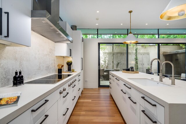 kitchen with white cabinets, hanging light fixtures, light hardwood / wood-style flooring, sink, and wall chimney range hood