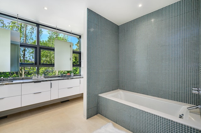 bathroom with tile patterned flooring, tiled tub, and vanity