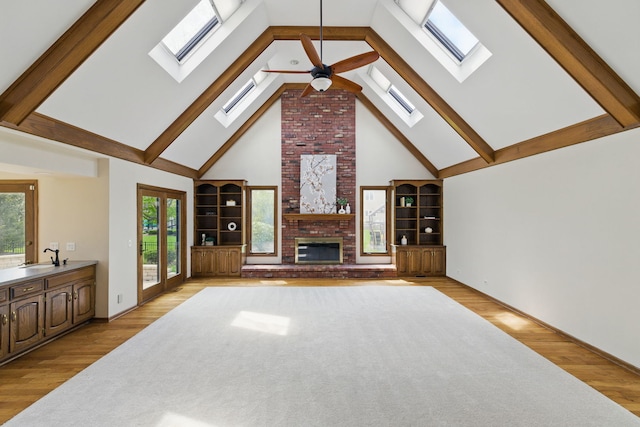 unfurnished living room featuring ceiling fan, a brick fireplace, high vaulted ceiling, light wood-style flooring, and a skylight