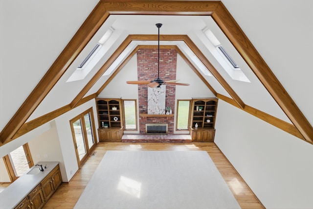 unfurnished living room featuring a ceiling fan, a skylight, a fireplace, a sink, and light wood finished floors